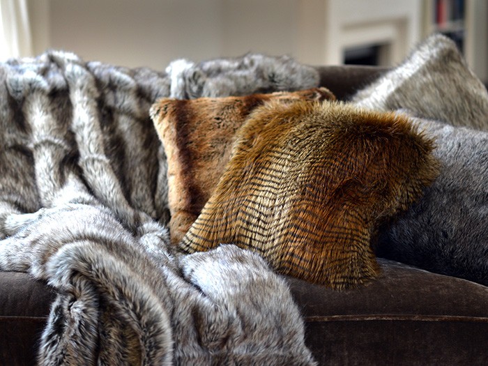 Faux fur throw blanket and faux fur accent pillows resting on a dark-colored sofa. 